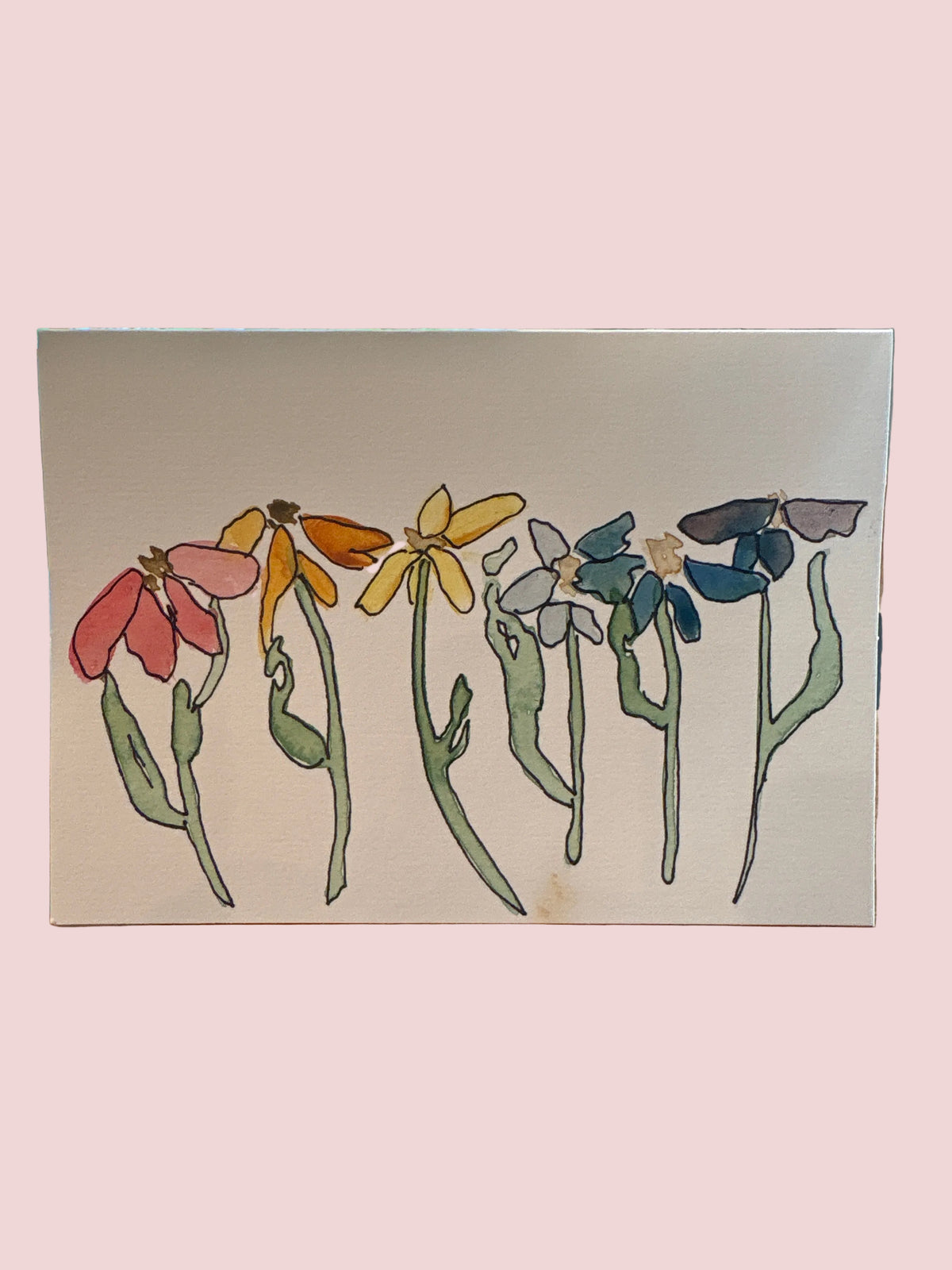 A square canvas art print featuring a colorful watercolor-style illustration of wildflowers, displayed on a wooden table in front of a window.